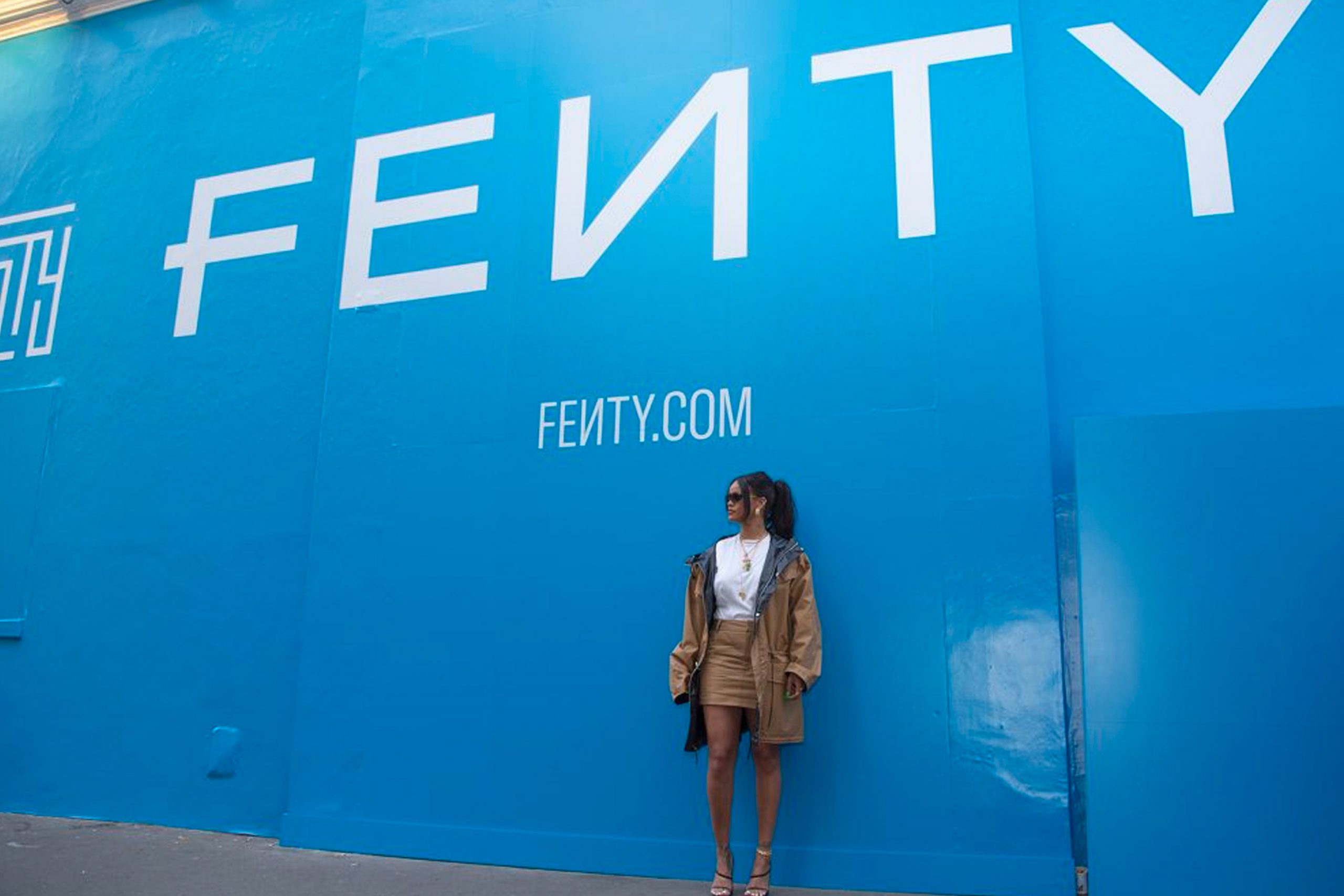 Rihanna standing in front of the blue FENTY poster